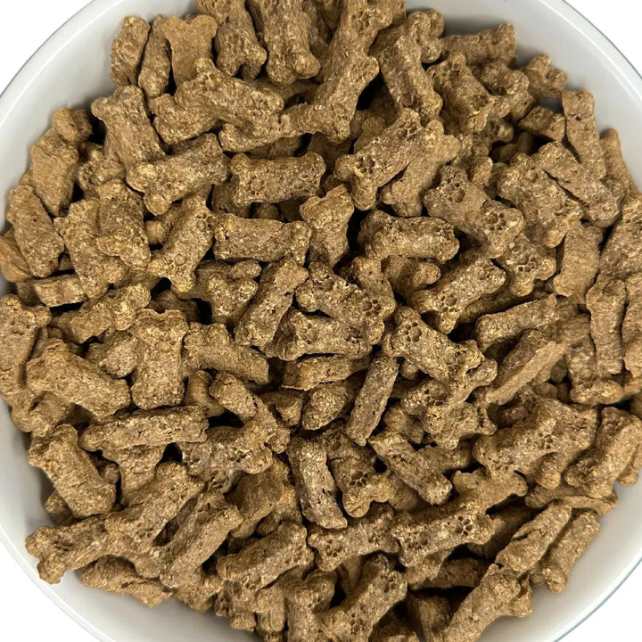 Close-up of bone-shaped Bacon bits dog treats in a white bowl