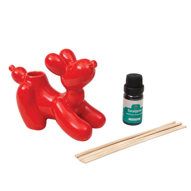 Red balloon dog-shaped diffuser with eucalyptus essential oil bottle and sticks on a white background
