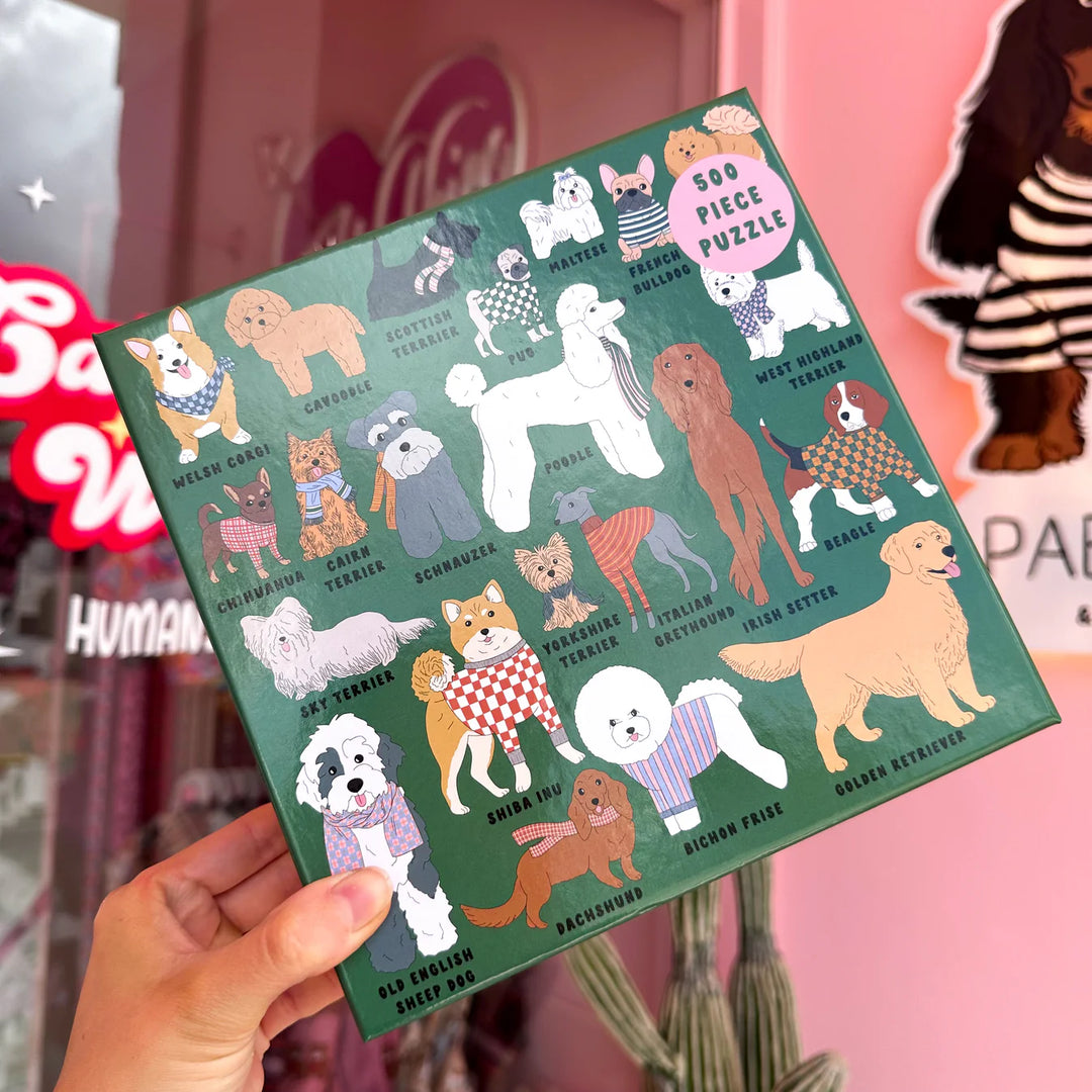 Hand holding a puzzle box with dog illustrations on a pink background