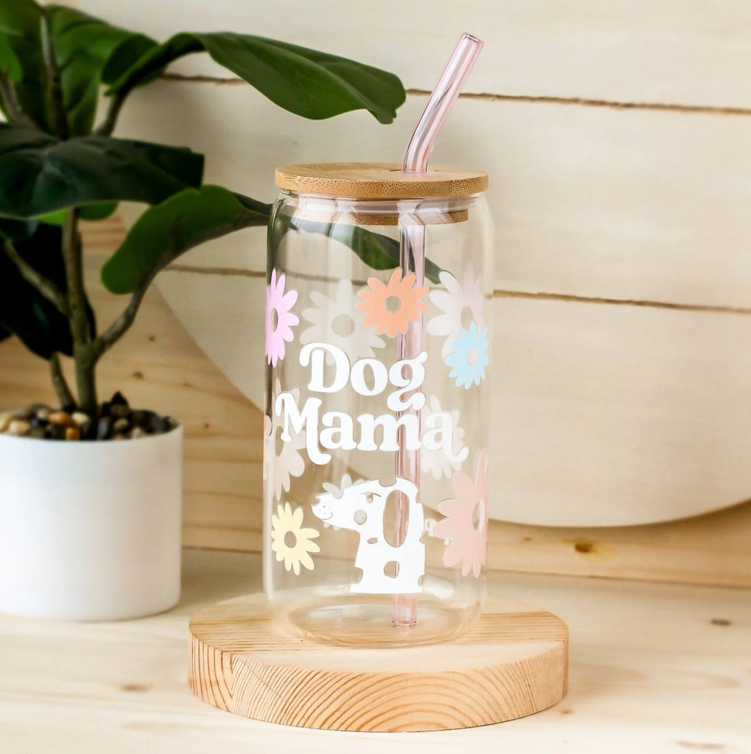 Clear tumbler with 'Dog Mama' text and floral designs on a wooden base with a plant in the background.