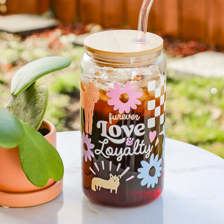 Glass tumbler with floral designs and text 'forever Love & Loyalty' on a blurred outdoor background