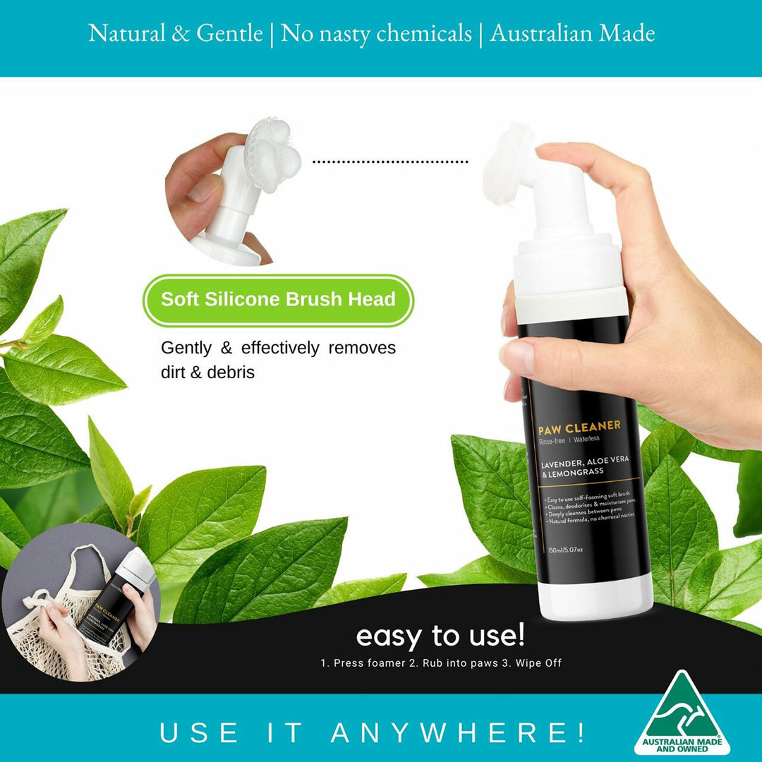 Paw cleaner with soft silicone brush head held by a hand, surrounded by green leaves.