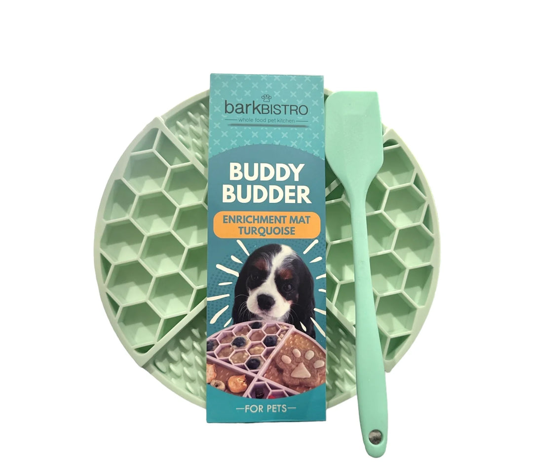 Green enrichment mat with a spoon and packaging labeled 'Buddy Budder' on a white background