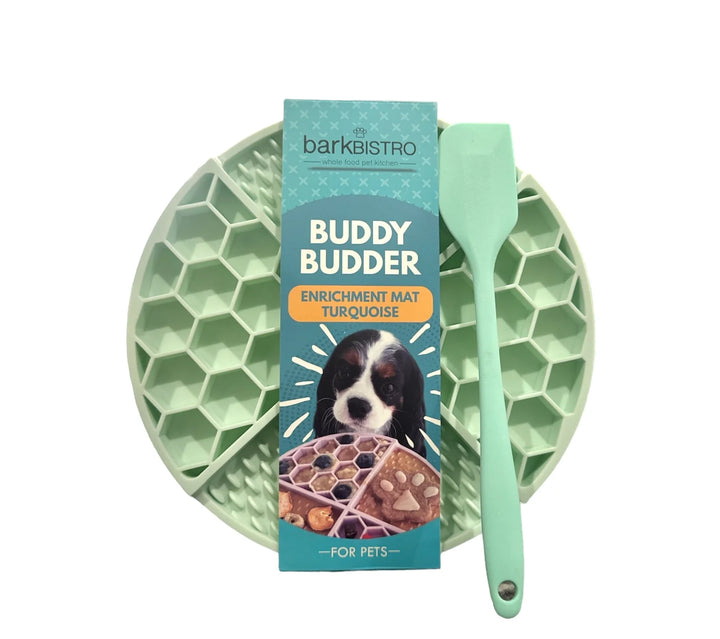 Green enrichment mat with a spoon and packaging labeled 'Buddy Budder' on a white background